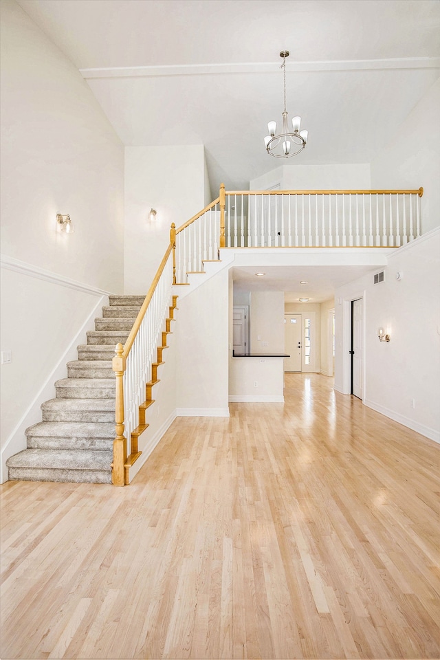 unfurnished living room featuring a towering ceiling, an inviting chandelier, and light wood-type flooring