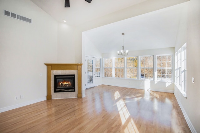 unfurnished living room with vaulted ceiling, ceiling fan with notable chandelier, a tile fireplace, and light hardwood / wood-style flooring