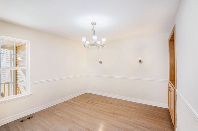 unfurnished room with a chandelier and light wood-type flooring