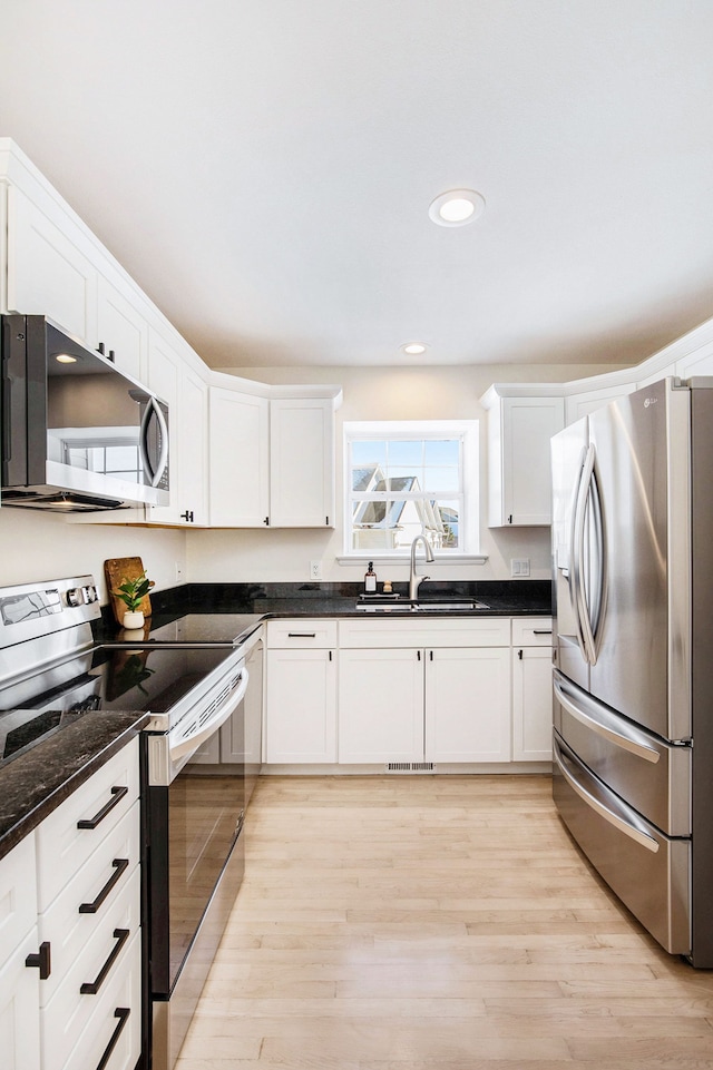 kitchen with sink, white cabinetry, dark stone countertops, appliances with stainless steel finishes, and light hardwood / wood-style floors