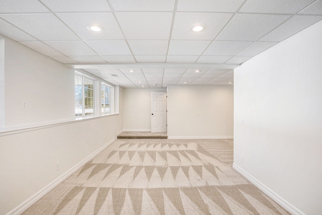 basement with a paneled ceiling and light colored carpet