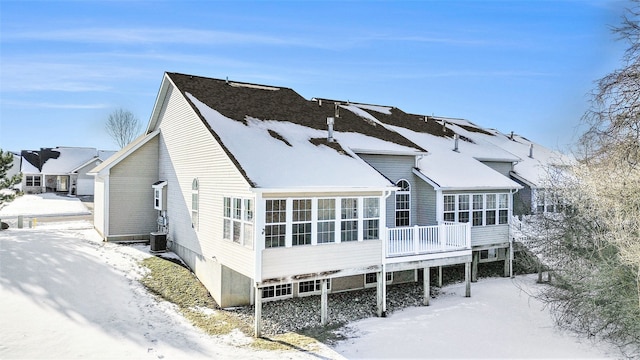 snow covered house featuring a wooden deck, central AC unit, and a sunroom