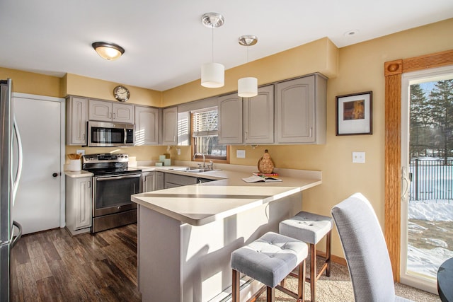 kitchen with sink, gray cabinetry, appliances with stainless steel finishes, kitchen peninsula, and pendant lighting