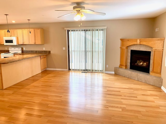 unfurnished living room with a tiled fireplace, baseboards, light wood-type flooring, and ceiling fan