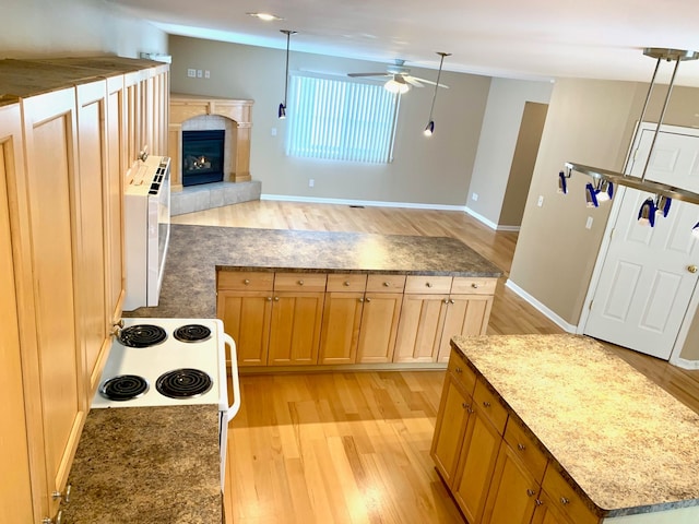 kitchen featuring open floor plan, a tiled fireplace, light wood finished floors, and a ceiling fan