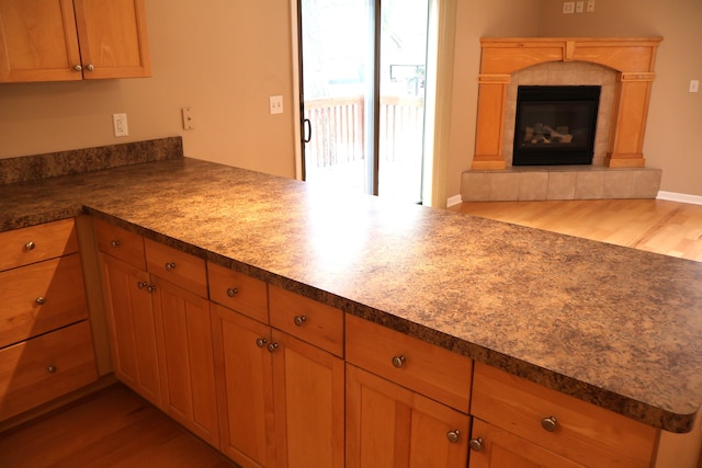 kitchen featuring a tile fireplace, open floor plan, a peninsula, and light wood-style floors