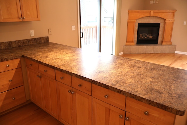 kitchen featuring a tile fireplace, a peninsula, light wood-style flooring, and open floor plan