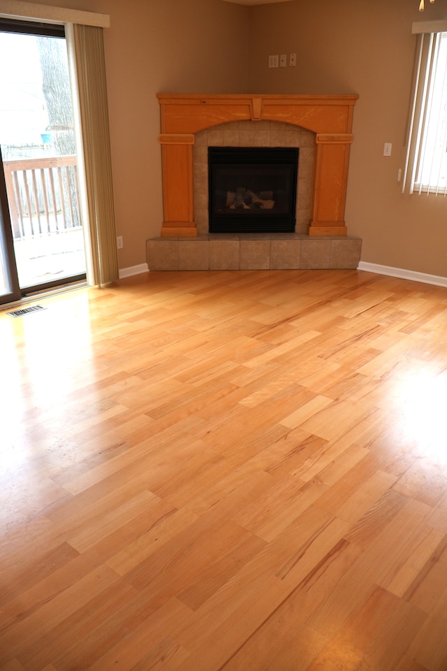 unfurnished living room with light wood-type flooring, visible vents, baseboards, and a fireplace