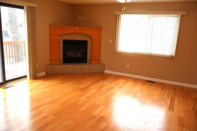 unfurnished living room featuring light wood-type flooring, a tile fireplace, visible vents, and a healthy amount of sunlight