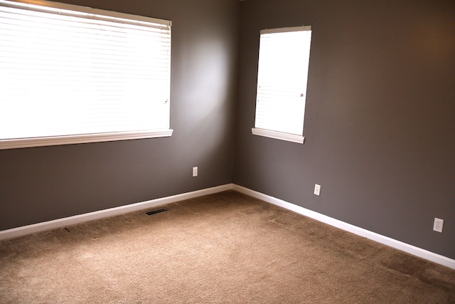 spare room featuring visible vents, baseboards, and dark colored carpet