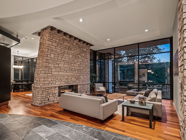 living room with wood-type flooring, a stone fireplace, a chandelier, and a wall of windows