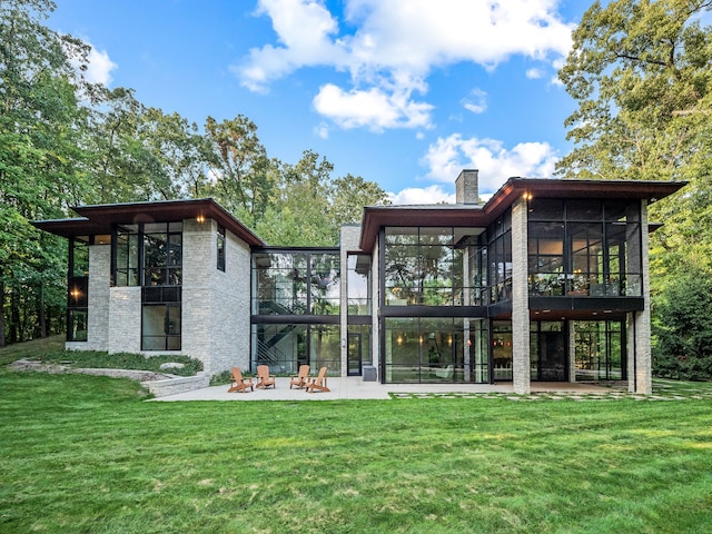 rear view of house with a patio, a sunroom, a lawn, and an outdoor fire pit