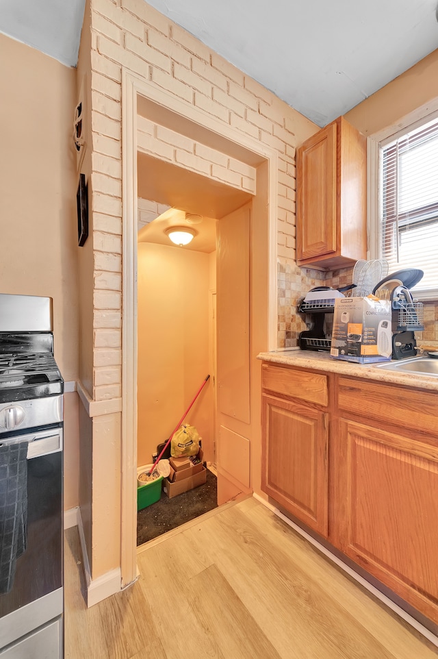 kitchen with tasteful backsplash, sink, stainless steel stove, and light wood-type flooring