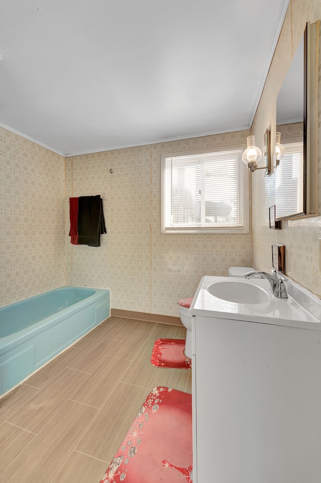 bathroom with vanity, a tub to relax in, toilet, and a healthy amount of sunlight