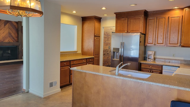 kitchen with visible vents, a large fireplace, brown cabinets, stainless steel fridge, and a sink