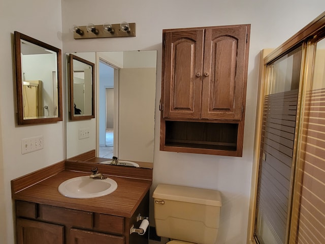 bathroom with toilet, vanity, and a shower with shower door