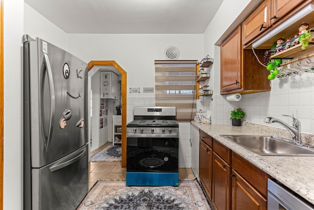 kitchen with appliances with stainless steel finishes, sink, backsplash, light tile patterned floors, and light stone countertops