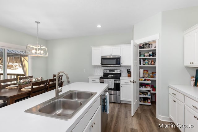 kitchen with dark wood-style flooring, a sink, hanging light fixtures, appliances with stainless steel finishes, and white cabinetry