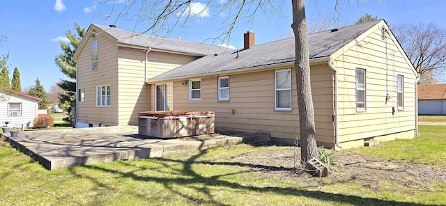 back of house with a chimney, a hot tub, a patio, a yard, and roof with shingles