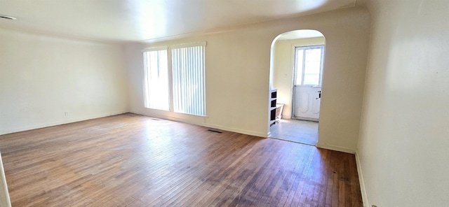spare room featuring arched walkways, hardwood / wood-style floors, and baseboards