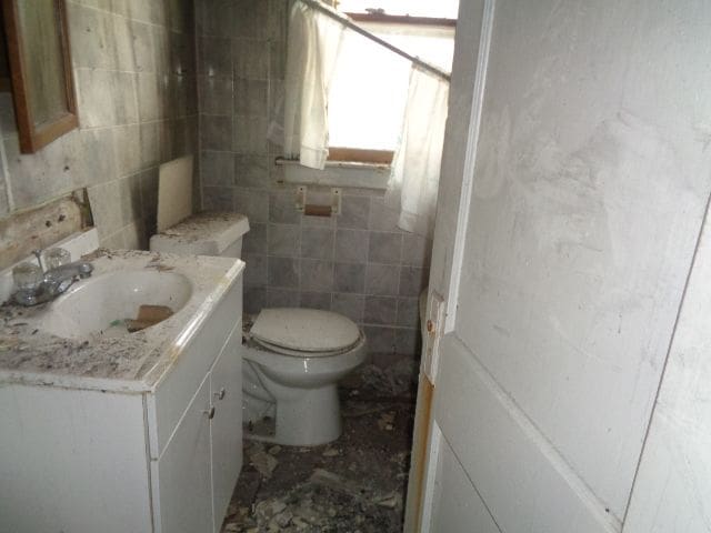 bathroom featuring vanity, toilet, and tile walls