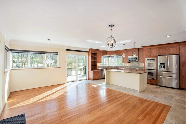 kitchen with appliances with stainless steel finishes, an inviting chandelier, hanging light fixtures, a center island, and light hardwood / wood-style floors