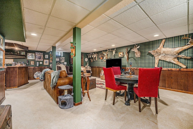 carpeted dining room featuring a paneled ceiling and wooden walls