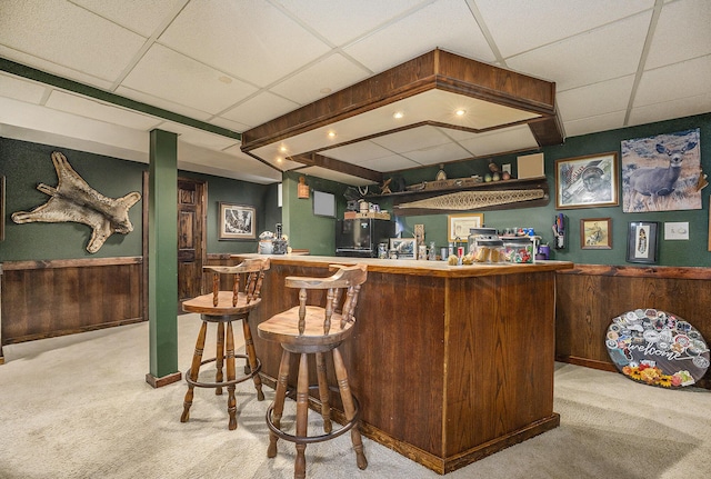 bar with light carpet, a paneled ceiling, and wooden walls