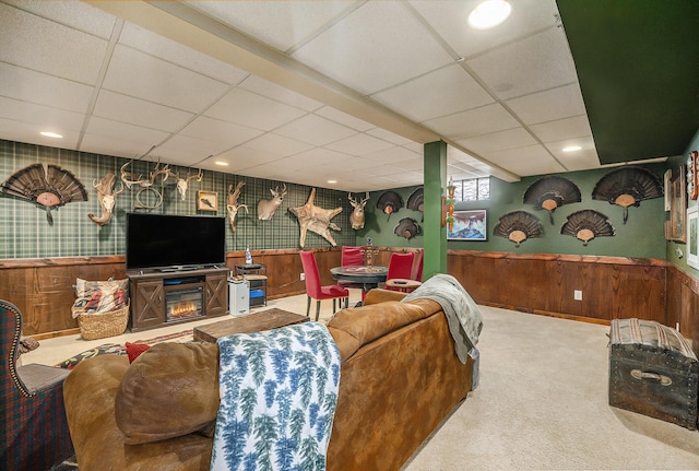 carpeted living room featuring a paneled ceiling and wood walls