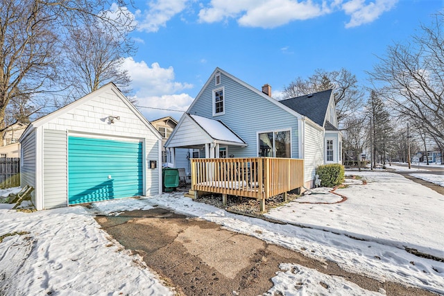 snow covered back of property with a garage, an outdoor structure, and a deck