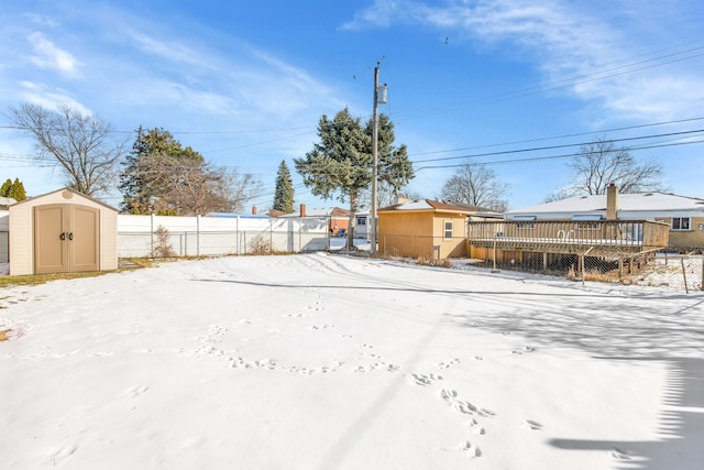 yard layered in snow featuring a shed and a wooden deck