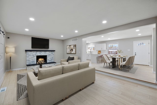 living room with a barn door, light hardwood / wood-style floors, and a stone fireplace