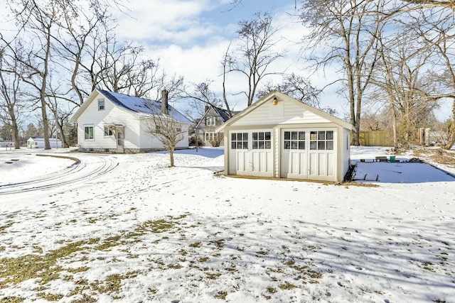 snow covered rear of property featuring a garage and an outdoor structure