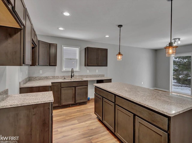 kitchen with pendant lighting, dark brown cabinetry, sink, and light hardwood / wood-style flooring