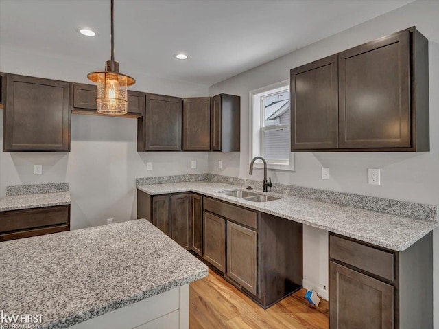 kitchen featuring pendant lighting, sink, dark brown cabinetry, light stone countertops, and light wood-type flooring