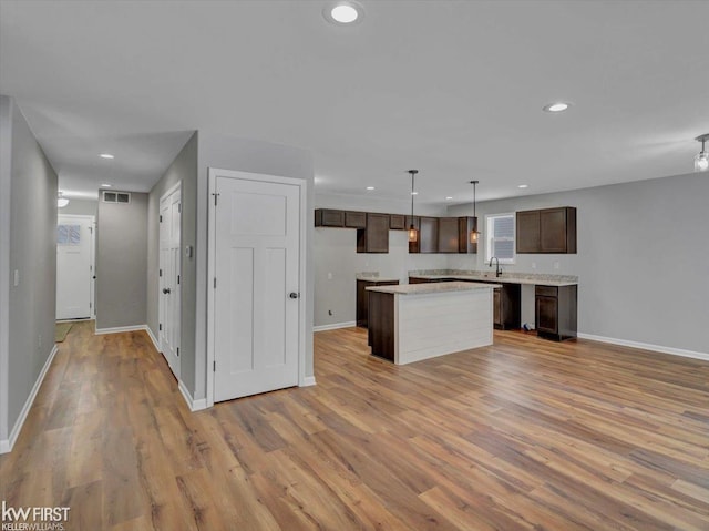 kitchen with a kitchen island, sink, hanging light fixtures, dark brown cabinets, and light hardwood / wood-style flooring