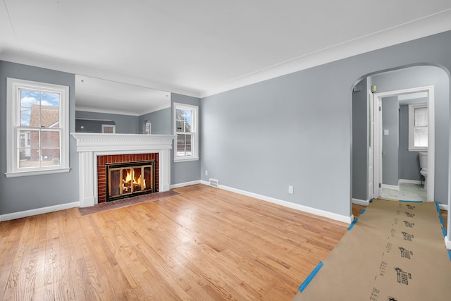 unfurnished living room featuring ornamental molding, plenty of natural light, a fireplace, and light hardwood / wood-style floors