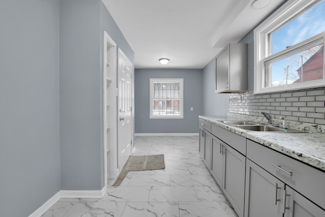 kitchen featuring sink, gray cabinetry, backsplash, and light stone counters