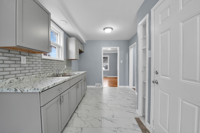 kitchen featuring gray cabinets, tasteful backsplash, sink, and light stone counters