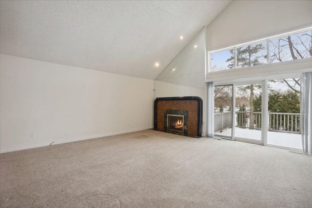 unfurnished living room featuring light colored carpet, a premium fireplace, and high vaulted ceiling