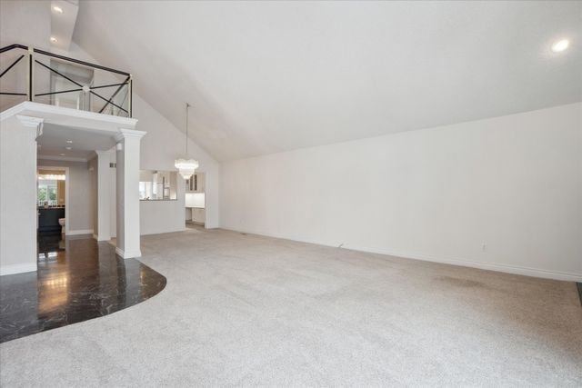 unfurnished living room featuring an inviting chandelier, carpet flooring, high vaulted ceiling, and ornate columns