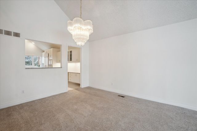 unfurnished living room featuring vaulted ceiling, light colored carpet, and an inviting chandelier