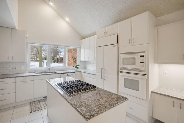 kitchen featuring sink, white cabinetry, built in appliances, a center island, and light stone countertops