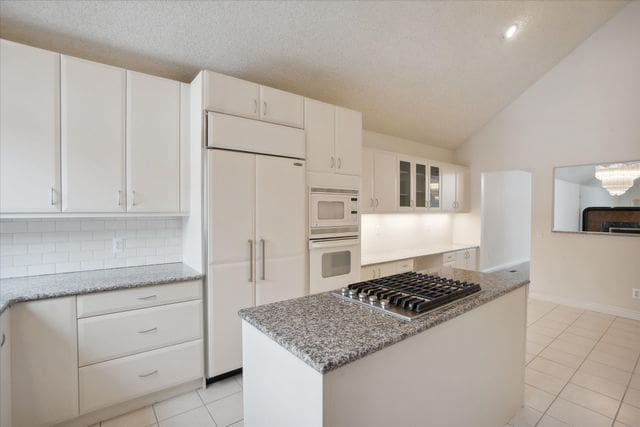 kitchen featuring white cabinetry, light stone counters, built in appliances, vaulted ceiling, and light tile patterned floors