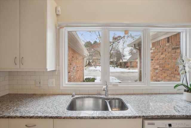 kitchen with white dishwasher, sink, white cabinetry, and light stone countertops