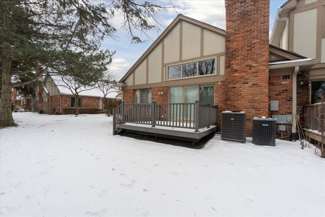 snow covered rear of property with central AC and a deck