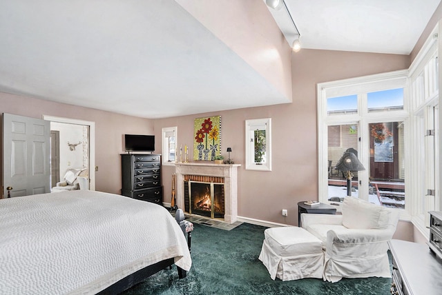 bedroom with vaulted ceiling, a brick fireplace, carpet flooring, and rail lighting