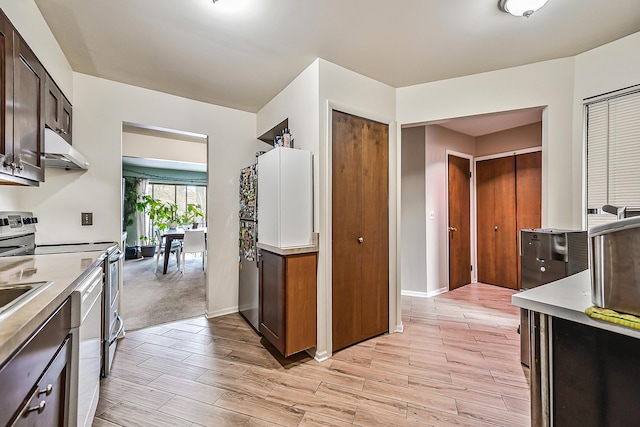 kitchen with under cabinet range hood, baseboards, stainless steel range with electric cooktop, light countertops, and light wood-type flooring