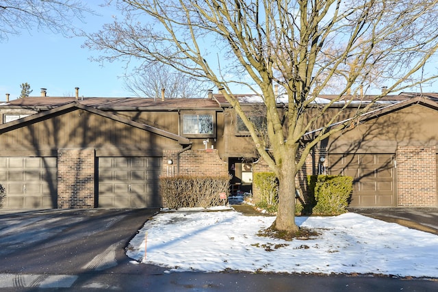 view of snowy exterior with a garage, brick siding, and driveway