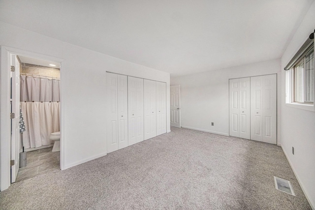 unfurnished bedroom with two closets, carpet floors, and ensuite bathroom